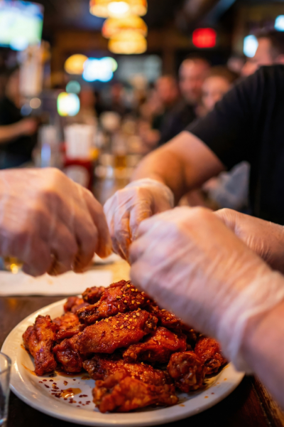 Hands grabbing hot wings off a plate at Greg's Burgers